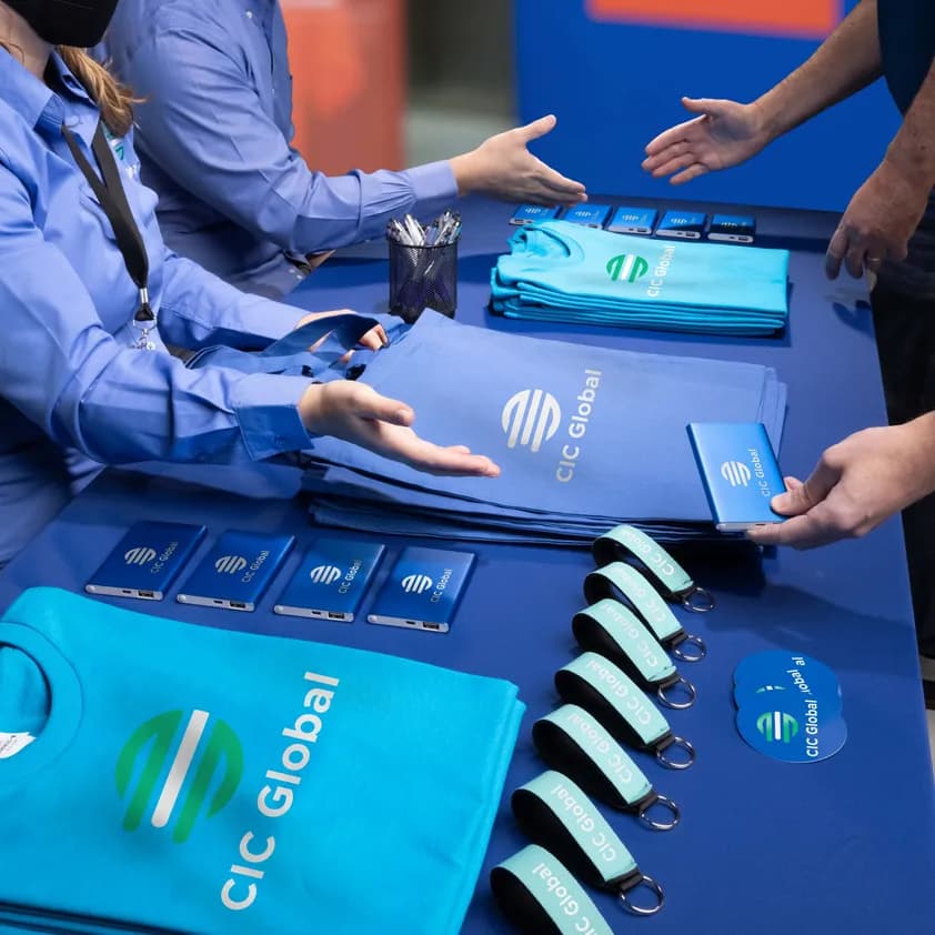 A tradeshow table with custom giveaways, including t-shirts, tote bags, power banks, keychains, pens, and stickers.