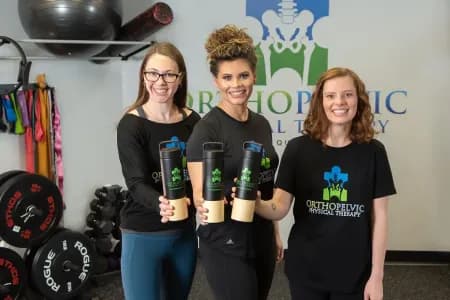 A group of doctors at OrthoPelvic Physical Therapy wear matching branded t-shirts and hold custom logo drinkware.