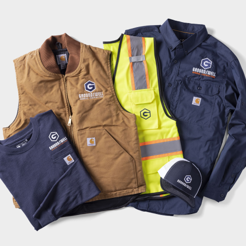 A safety vest and a Carhartt vest, jacket, and t-shirt are customized with a construction logo.